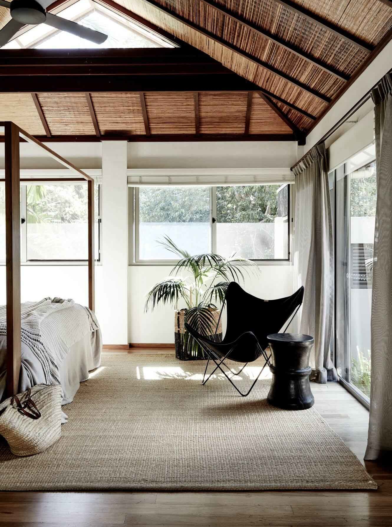 Master bedroom at The Villas of Byron with beautful natural light, textured rug, butterfly chair, four poster bed and views of the Byron bushland