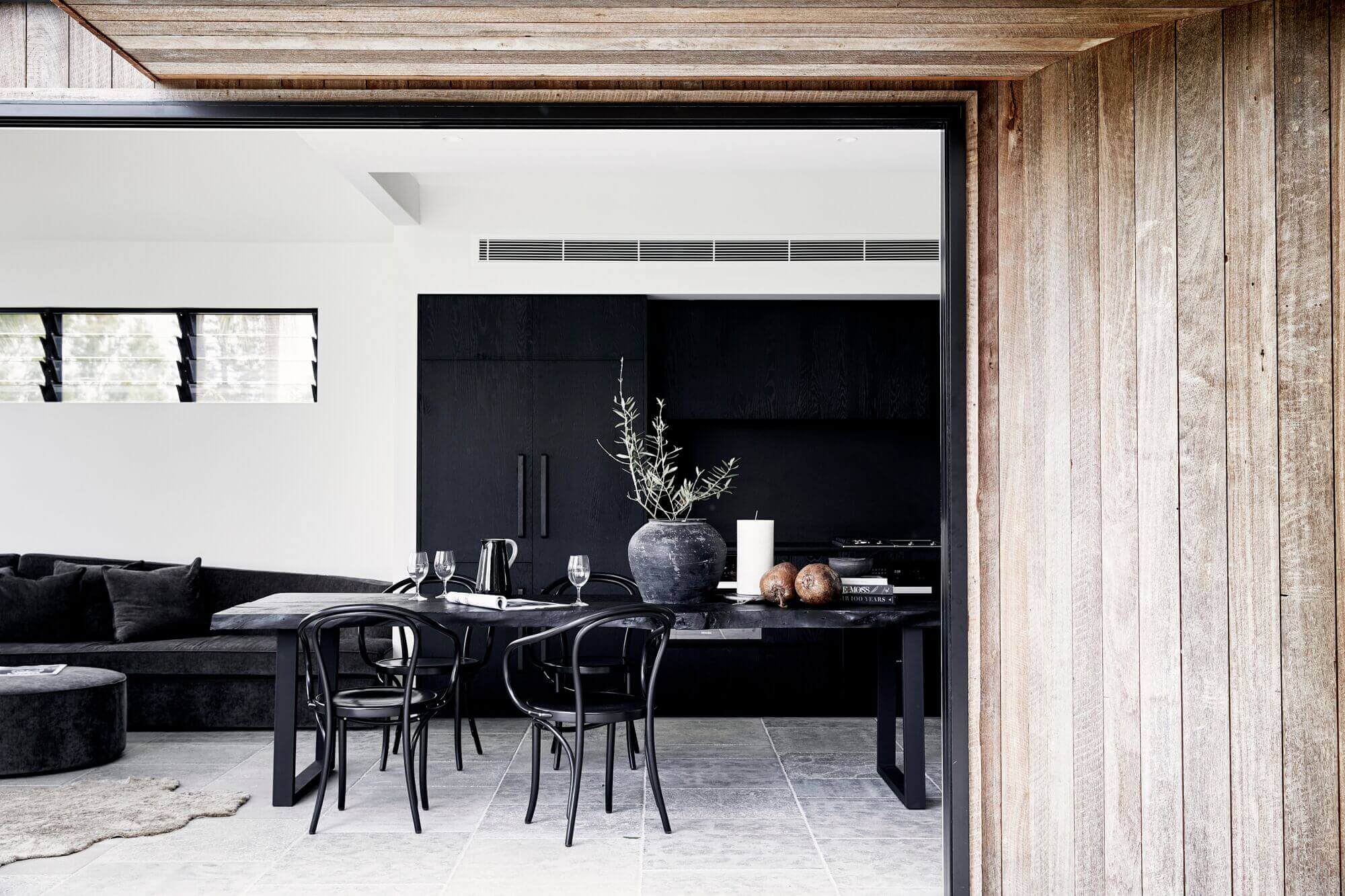 Kitchen and dining room at The Cabin, Byron Beach Abodes, with custom timber dining table, Bentwood dining chairs and black Oak cabinetry