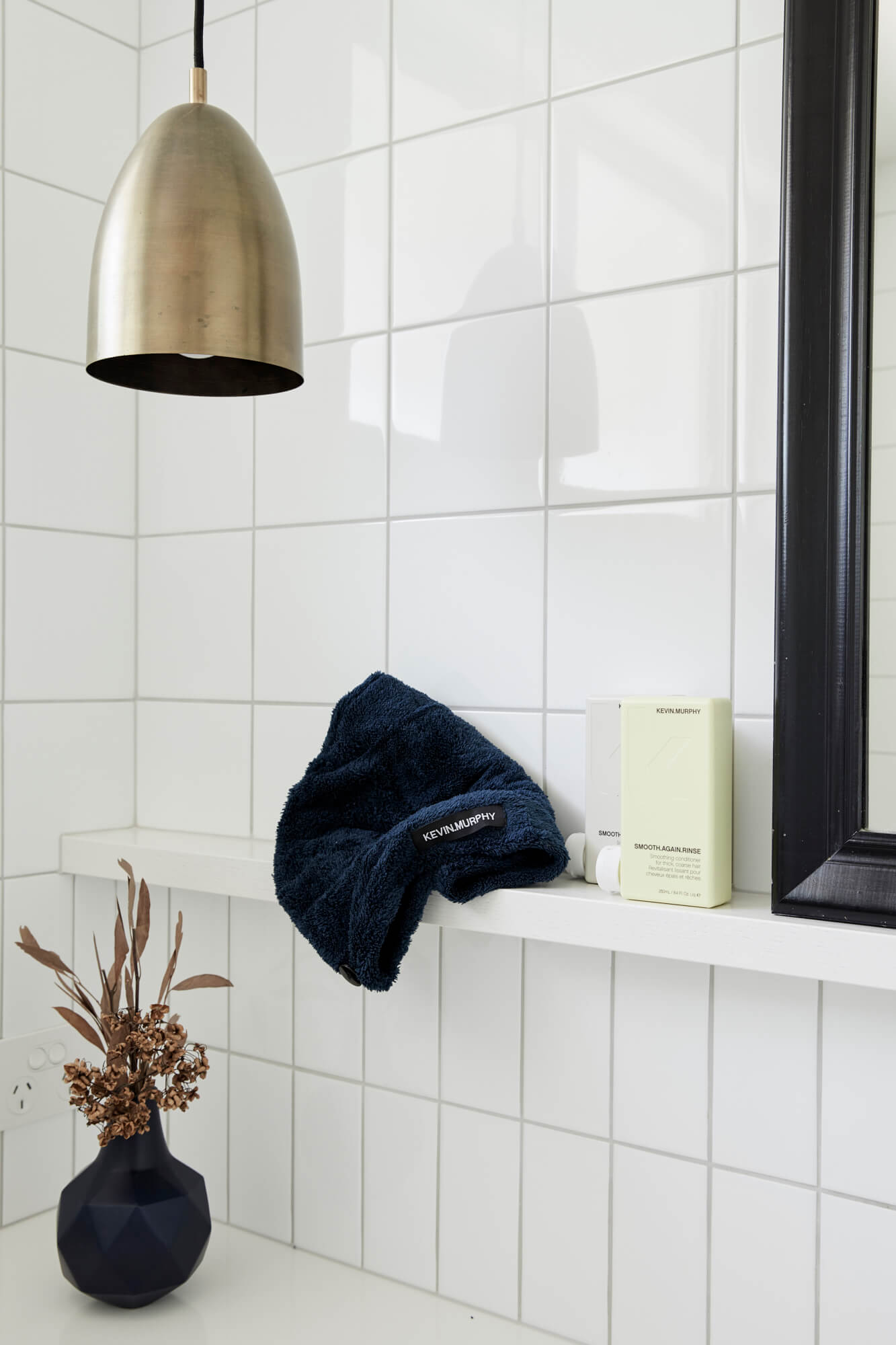 Bathroom with white gloss tiles, wall shelf with Kevin Murphy products, and hanging brass light at the Bower Suites, The Bower Byron Bay hotel