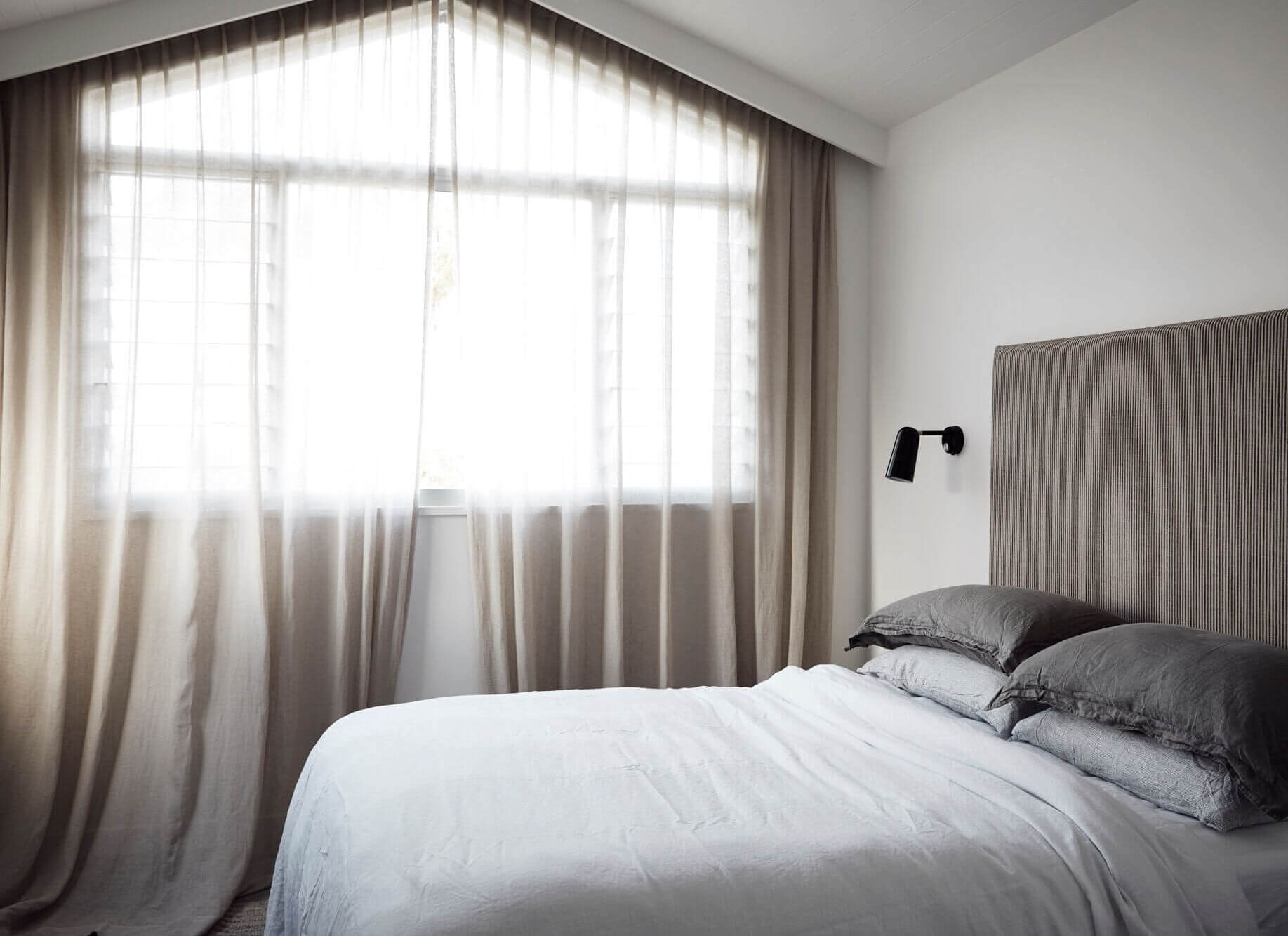 Bedroom at The Lodge, Byron Beach Abodes with muted colour palette, luxury bed linen, fabric covered bedhead and sheer linen curtains
