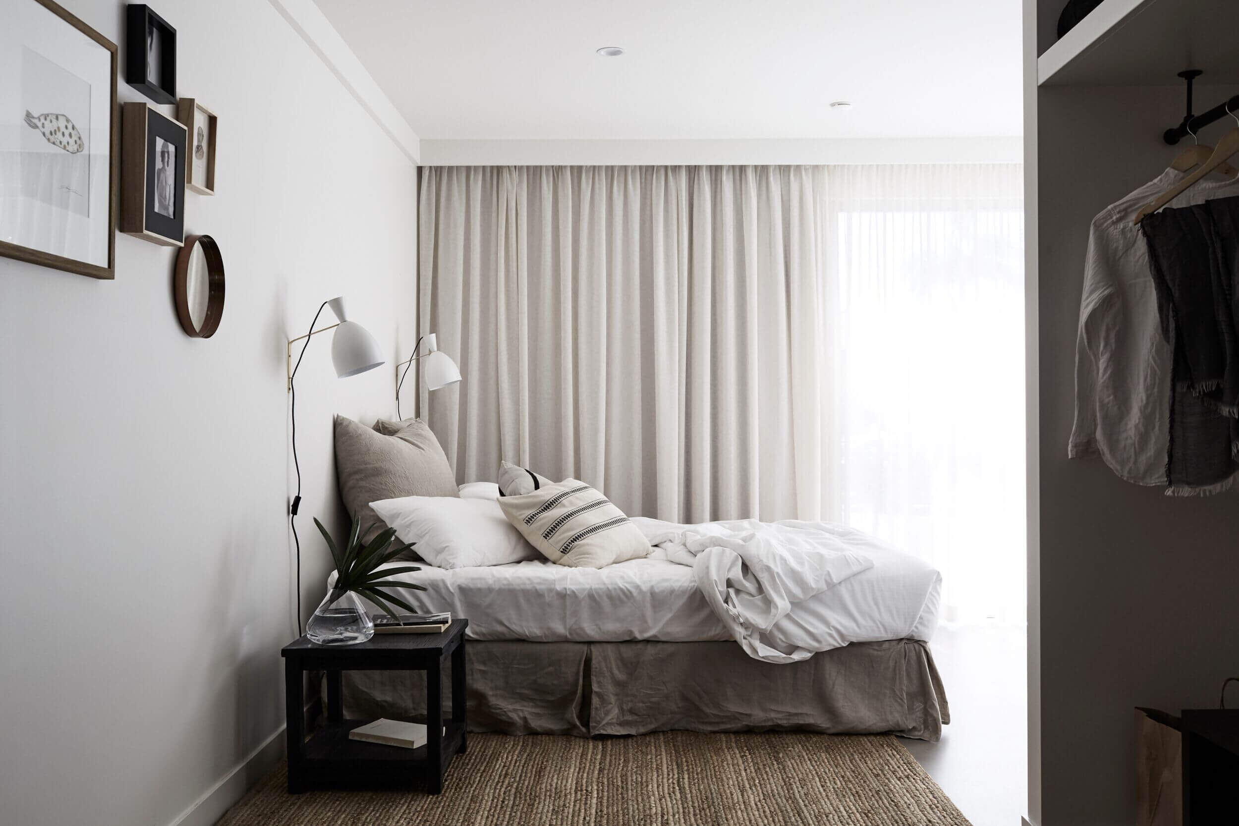 Stylish accommodation with sisal rug, soft bed with layers of linen and cushions in muted colours, white wall lights and draped linen curtains
