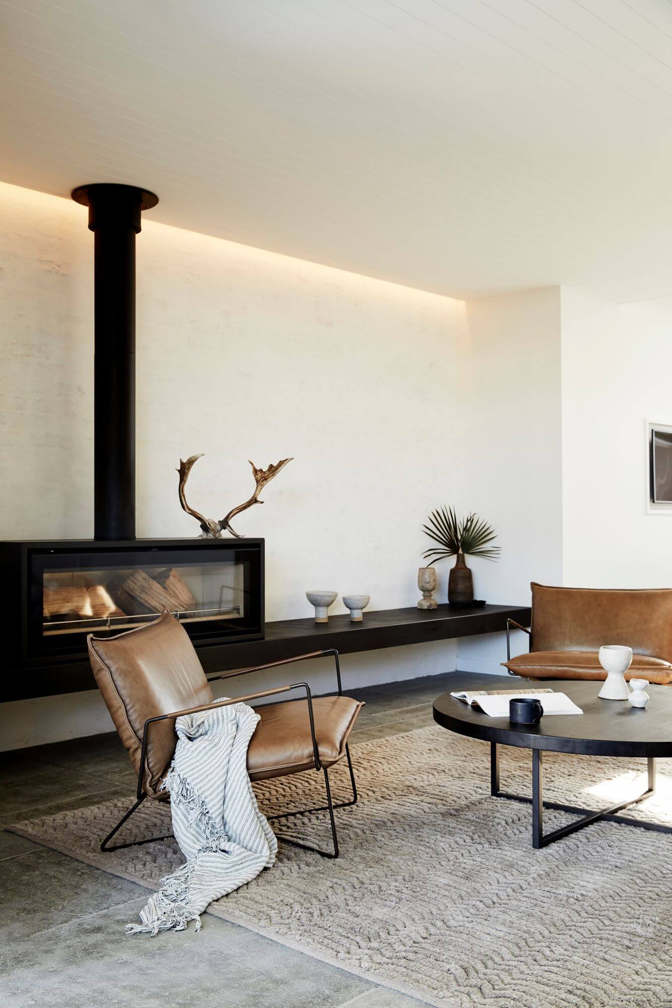Lounge room at The Lodge, Byron Beach Abodes with rendered walls, soft strip lighting, fireplace, and leather armchairs